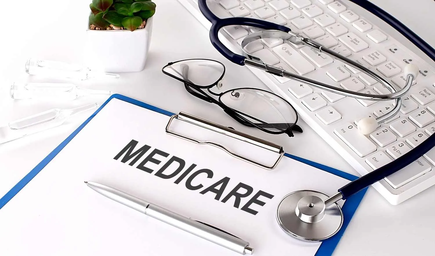 Clipboard marked Medicare on a desk beside glasses, a pen and a stethoscope