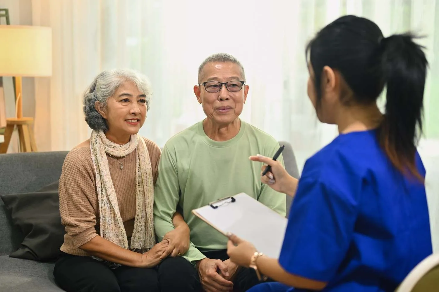 Older couple on a sofa talking through their Medicare options with someone holding a clipboard
